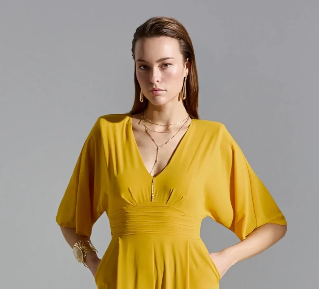 Mujer con mono amarillo de invitada de boda y collar en forma de T elegante